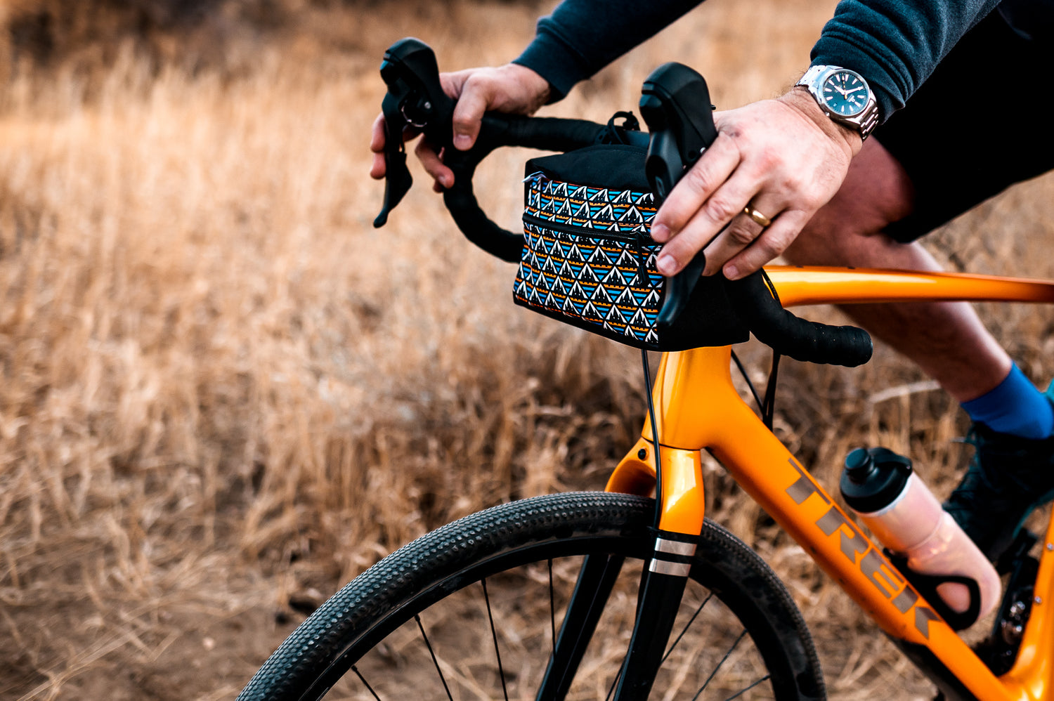 A close up shot of an orange and blue mosaic patterned bicycle handlebar bag on an orange gravel bicycle